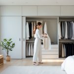 A woman choosing clothes from a neatly organized minimalist wardrobe in a bright bedroom with natural light.